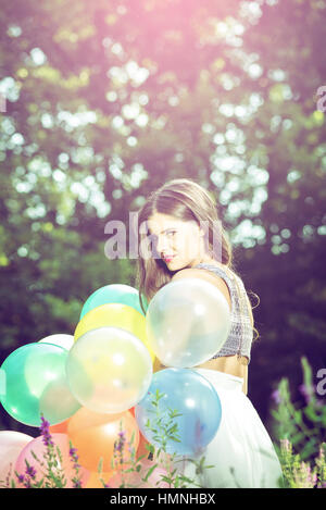 Girl posing in nature with balloons. View from behind. Toned image. Vintage retro look. Stock Photo