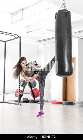 Attractive brunette female doing kickboxing high kick exercise in modern fitness center. Stock Photo