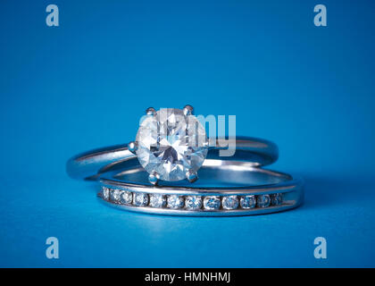A diamond solitaire engagement ring stacked on a diamond wedding band against a blue background Stock Photo