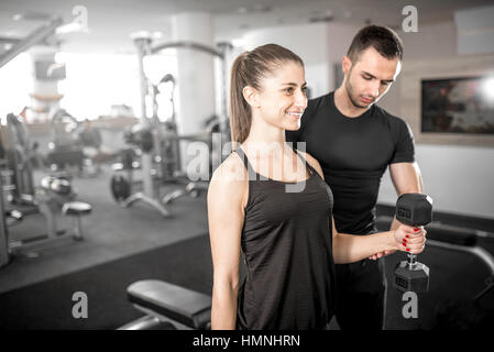 Young adult woman working out in gym, doing bicep curls with help of her personal trainer. Stock Photo
