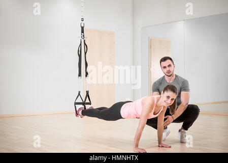 Young adult girl doing suspension rope exercise together with her personal private coach. Stock Photo