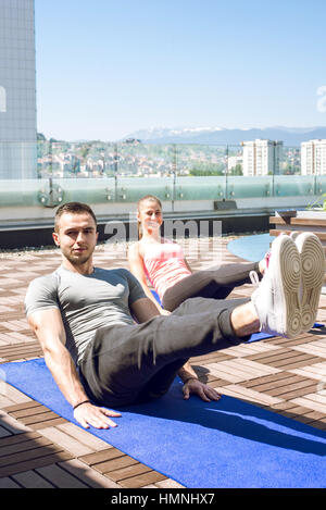 Young fitness couple doing legs up crunches outdoor on rooftop. Stock Photo