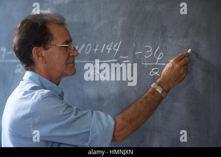People and education. Teacher writing on math equation on blackboard during lesson. Stock Photo