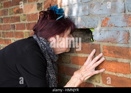 Woman looking through a hole in a brick wall Stock Photo