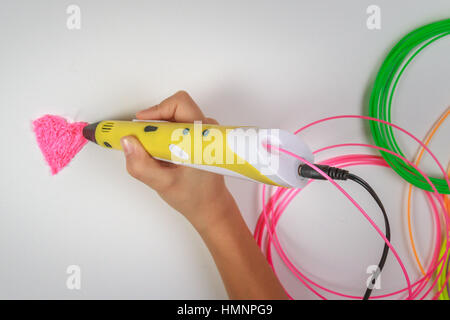 Kids hand holds yellow 3D printing pen with filaments on white background. Stock Photo