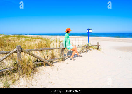 Young woman sitting on wooden fence of entrance to Lubiatowo beach, Baltic Sea, Poland Stock Photo