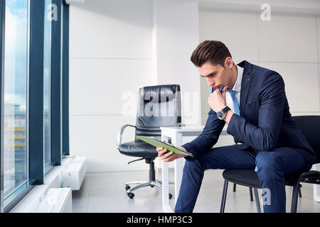 Businessman with pen in hand reading, thinking over contract pap Stock Photo