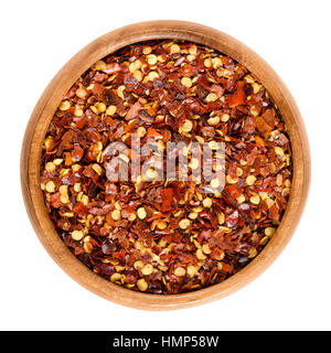 Dried chili pepper flakes in wooden bowl. Dried and crushed fruits of Capsicum frutescens, used as hot spice and for tabasco sauce. Isolated macro foo Stock Photo
