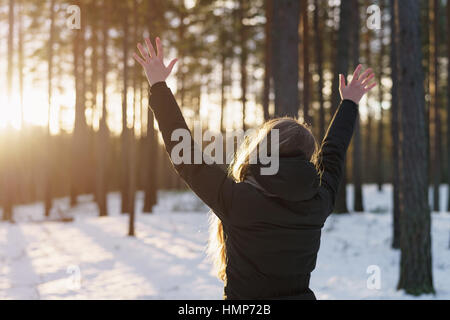 teen girl raised hands from behind in winter pine forest in sunset Stock Photo