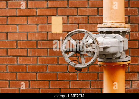 Gas valve on yellow natural gas distribution industrial pipe in front of red brick wall with copyspace Stock Photo