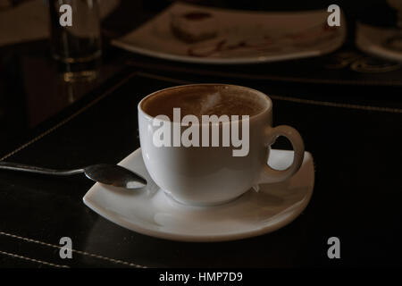 Side view of cappuccino cup on table in dark cafe room Stock Photo