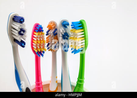 Close up shot of set of multicolored toothbrushes in glass on clean toilet on white background, concept dental. Stock Photo