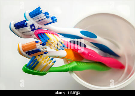 Close up shot of set of multicolored toothbrushes in glass on clean toilet on white background, concept dental. Stock Photo