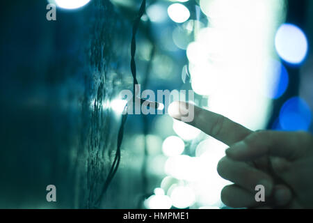front view close up of finger touching a lone bright led light with city lights in the background, concept for connection, communication Stock Photo