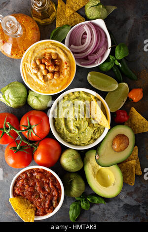 Homemade hummus, salsa and guacamole with corn chips and vegetables overhead view Stock Photo