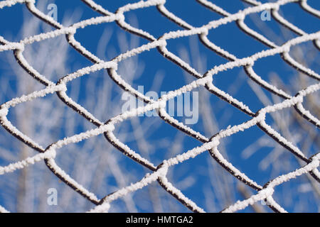 front view of frozen metallic fence texture pattern with blue sky and trees in the background and selective focus Stock Photo