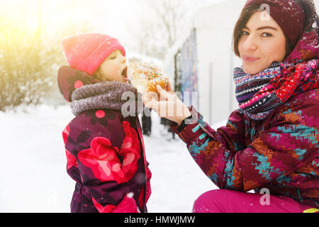 Mum feeds girl with bun on winter walk Stock Photo