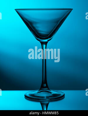 A martini glass sat on a mirror.   Stobist: Yongnuo 560III flash, with a 7" gridded reflector and green gel, lighting the white wall behind. The glass Stock Photo