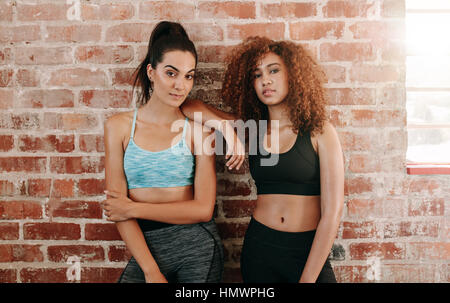 Portrait of sporty young woman standing against wall. Two fitness females in gym after workout.