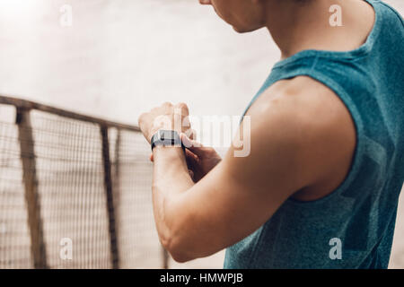 Close up shot of young man outdoors using a smartwatch to monitor his progress. Male runner resting and checking his performance on smart watch device Stock Photo