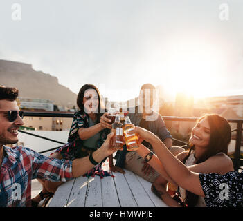 Young friends hanging out and enjoying drinks on rooftop. Young people at party toasting beers. Stock Photo