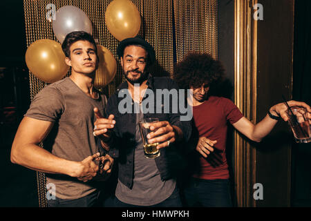 Portrait of three young men having fun at the nightclub. Group of men at pub with drinks. Stock Photo