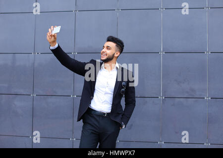 Entrepreneur takes makes selfie man male looking at camera and smiling talks on mobile smart phone. Young handsome businessman arab muslims in busines Stock Photo