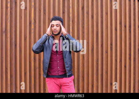Handsome Young Arabic Male Man, Student Feels Headache, Touching Head, Trying to Ease Pain, Feels Discomfort, Standing on Background of Wooden Panel S Stock Photo