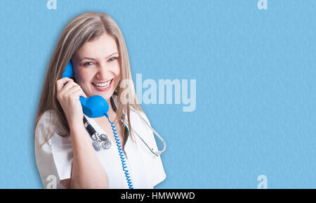 Smiling and friendly medical doctor with telephone having fun on blue background with text area Stock Photo