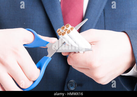 Close-up of man in suit cutting bunch of cigarettes with scissors isolated on white background Stock Photo