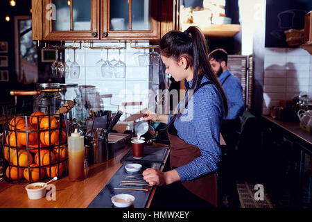 The bartender barista girl makes hot milk at the bar in cafe res Stock Photo