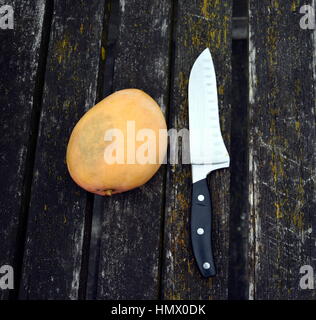 Mango and a big knife on an old weathered deck wooden board. Vertical wood background texture. Stock Photo