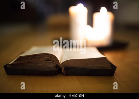 Bible laid on wooden floor, burning candles in the background Stock Photo