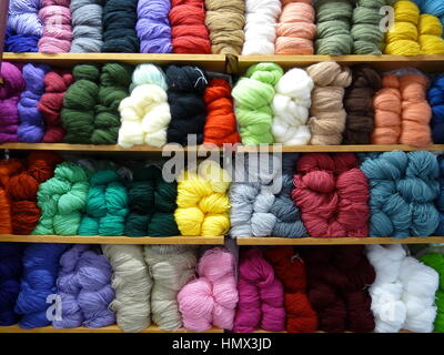 Shelves full of rows of brightly-coloured skeins of yarn or balls of wool in a variety of colours in a craft shop Stock Photo