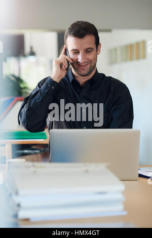 Smiling businessman using a laptop and talking on the phone Stock Photo