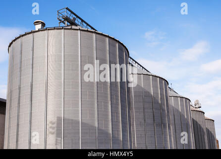 Agricultural Silos. Building Exterior. Storage and drying of grains, wheat, corn, soy, sunflower against the blue sky with white clouds Stock Photo