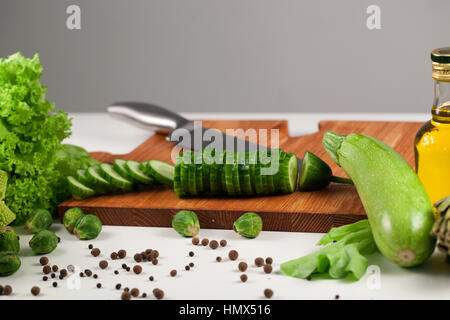 Sliced cucumber in stack on the wooden cutting board among vegetables Stock Photo