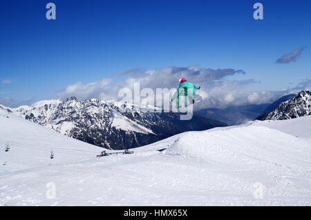 Snowboarder jumping in snow park at winter mountain on nice sunny day. Caucasus Mountains, region Dombay. Stock Photo