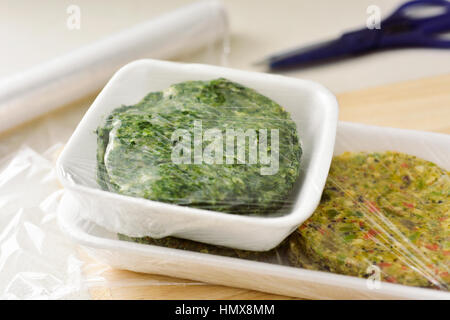 closeup of some different raw veggie burgers in plastic trays covered with plastic wrap ready to be introduced in the fridge or in the freezer Stock Photo