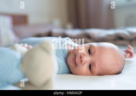 Cute newborn baby boy with teddy bear lying on bed Stock Photo