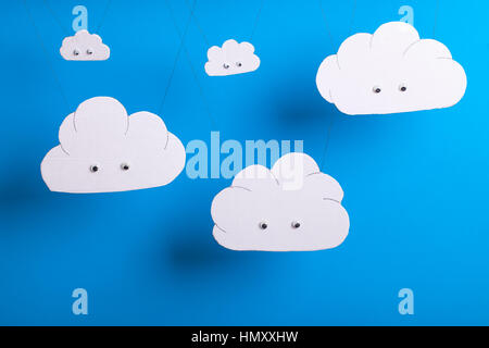 Cloud computing concept with white cardboard cutout cute clouds with eyes hanging in front of a sky blue background. Stock Photo