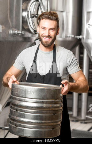 Worker carrying barrel with beer at the brewery with metal containers on the background Stock Photo