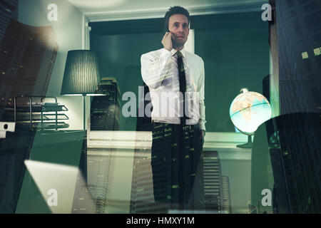 Serious business man talking on phone at office with city in background, working overtime at night Stock Photo