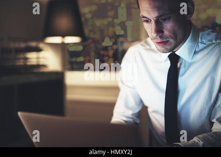 Serious businessman working on laptop at night sitting in office looking concentrated Stock Photo