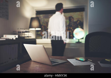 Serious businessman thinking standing in office at night looking out window Stock Photo