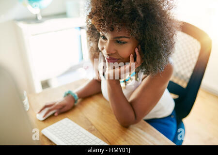 Young pretty afro-american girl working on pc and smiling on blurred inside background. Stock Photo