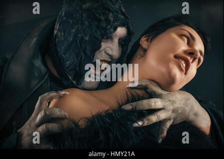 Scary vampire devil biting young woman. Medieval gothic nightmare horror. Studio shoot Stock Photo