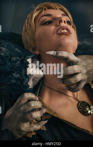 Scary vampire devil biting young woman. Medieval gothic nightmare horror. Studio shoot Stock Photo