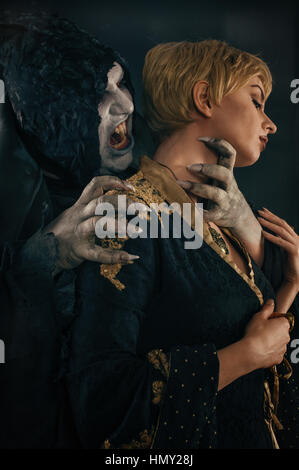 Scary vampire devil biting young woman. Medieval gothic nightmare horror. Studio shoot Stock Photo