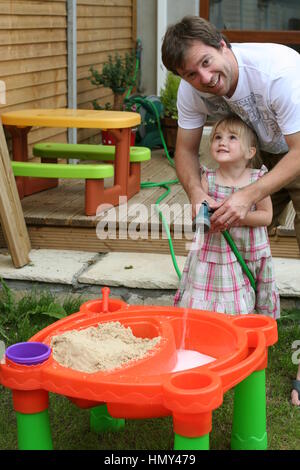 Summer fun, little girls playing with water and sand in a sandpit in the garden, Ireland father daughter concept Stock Photo